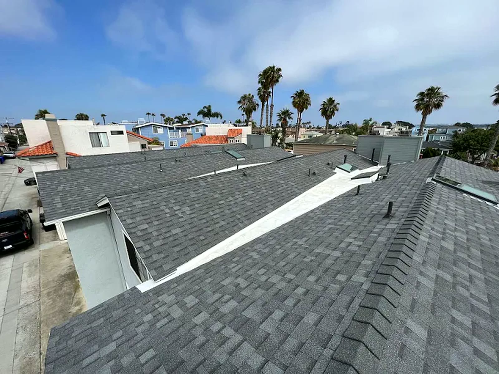 Completed gray asphalt shingle roof over a San Diego home, with the coastal skyline and palm trees behind it