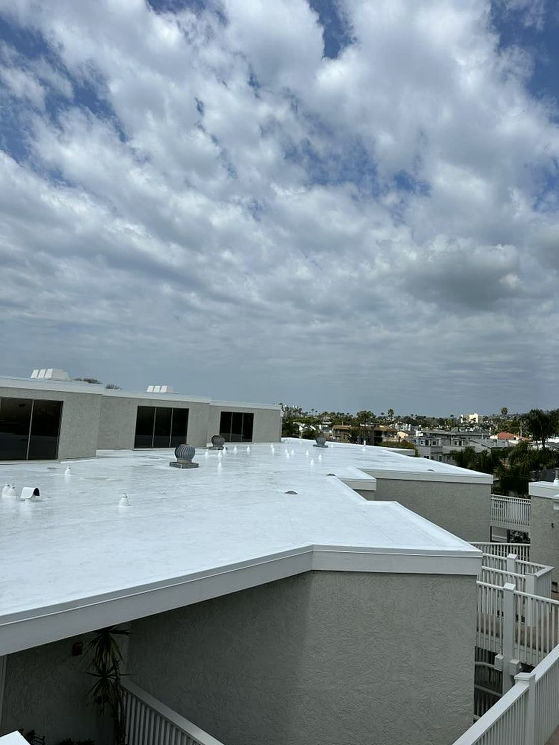 Freshly applied white reflective waterproof coating on a flat commercial roof under dramatic clouds